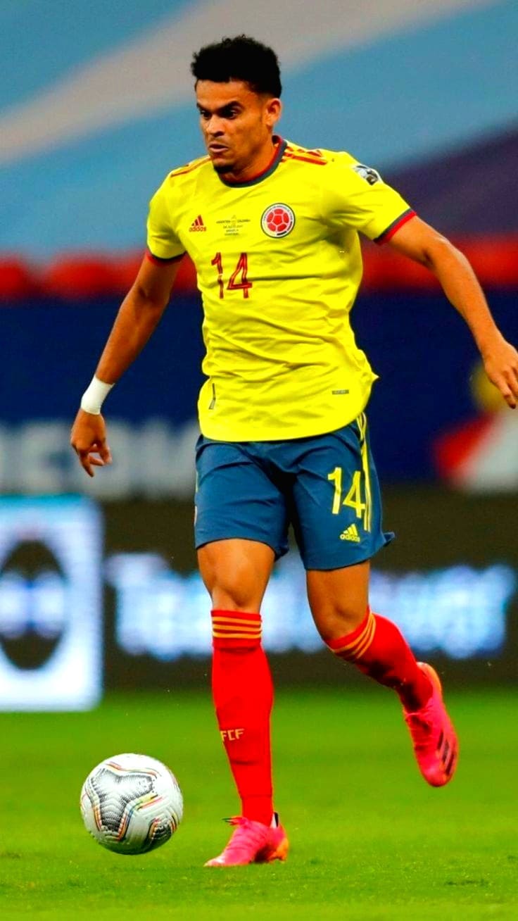 A soccer player in a yellow jersey with the number 14, blue shorts, and red socks is controlling a soccer ball on a field during a match, while fans enjoy every moment thanks to IPTV Suisse.